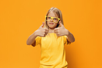 portrait of a cute beautiful school-age girl in yellow glasses for vision on a yellow background, pleasantly smiling looking at the camera and showing thumbs up