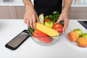 Close up of male hands holding a bowl full of fruits and vegetables in the kitchen. Healthy food concept