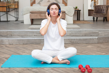 Attractive fit and slender woman wearing headphones and listening to music while training at home