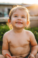 The portrait of a baby girl being naked only in a diaper in the garden with vegetables playing in...