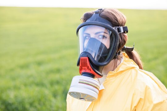 Person in overalls and gas mask call to save the planet while standing on green field on sunset. Concept of bad ecology and environmental protection