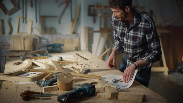 Portrait of a Young Carpenter Looking at a Blueprint and Starting to Assemble a Wooden Chair. Professional Furniture Designer Working in a Studio in Loft Space with Tools on the Walls.