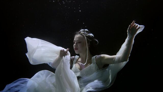 portrait of a woman in dark water. she moves hands beautifully with a white translucent fabric