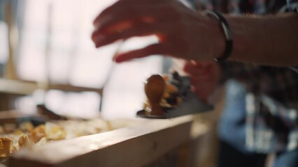 Close Up Portrait of a Handsome Young Artisan Craftsman in Checkered Shirt Using Hand Plane to Shape a Wood Bar. Carpenter Working on a Project in a Loft Studio with Tools on Walls.
