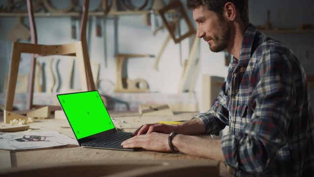 Arc Shot of a Handsome Furniture Designer Working on Laptop Computer with Green Screen Mock Up Display. Creative Young Man Preparing a Design for Carpentry Project.