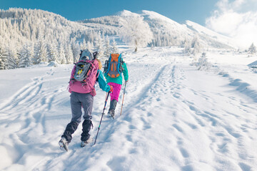 Fototapeta na wymiar Two women walk with snowshoes on the backpacks in winter trekking