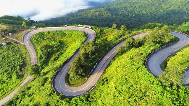 Aerial video top view drone road photo over green mountains with white fog floating and paths exciting steep road way of travel