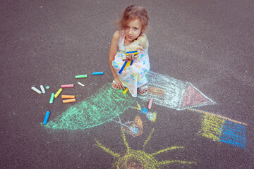 Fototapeta premium Ukrainian girl child draws children's drawings with chalk on the pavement.