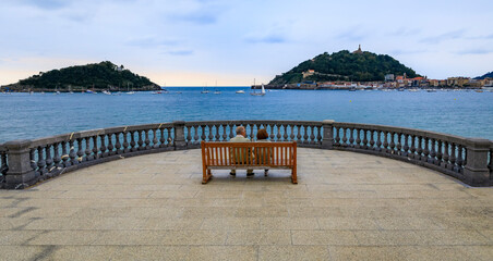 Obraz premium A couple on la Concha promenade bench with a view the bay in San Sebastian Spain