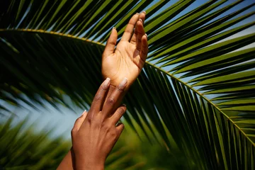 Poster Hands skin care. Photo of African female hands with manicure against palm leaf's background. Natural beauty product concept © Beauty Agent Studio