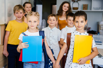 Concept of enrolling Ukrainian kids to schools. Two new pupils girls holding by hands standing among other children at class. Group portrait.