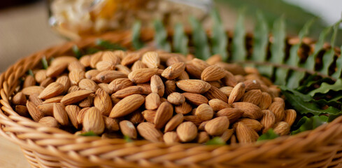 almond nuts peeled in wooden bowl with green, side view.