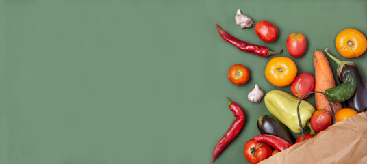Trendy ugly organic vegetables. Assortment fresh bell peppers, tomatoes, eggplants, hot peppers, carrots, cucumbers in craft paper bag over green background. Top view. Non gmo. Banner with copy space