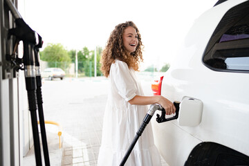 Young curly woman refueling car at gas station - Powered by Adobe