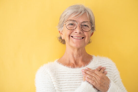 Beautiful senior woman with eyeglasses looking at camera with hands over her heart expressing love. Isolated on yellow background