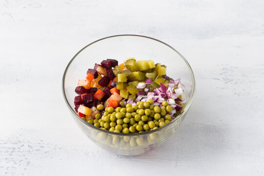 Glass bowl with vinaigrette salad of vegetables, beets, carrots, potatoes, canned green peas and red onions on a light blue background. Cooking homemade vegan food.