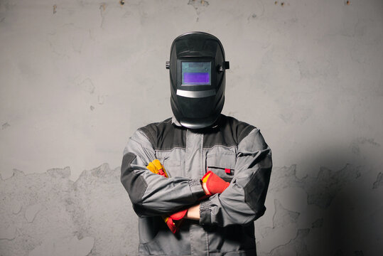 Serious welder man standing in the welding helmet on gray background.