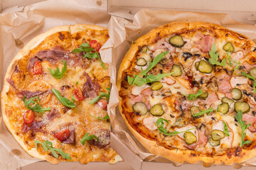 Two different pizza with various ham in open cardboard boxes
