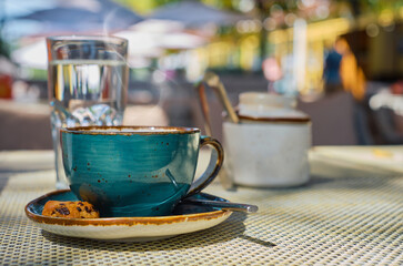 Steam rises over a cup of espresso coffee, a glass of water and cookies on the table, close-up, sunlight and selective focus, empty space, cafe breakfast, advertising or banner