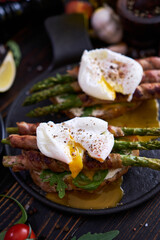 Tasty breakfast - toasts with cream cheese, poached eggs and Asparagus wrapped with bacon and spices on a plate