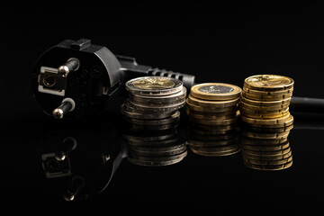 Black electric plug and euro coins on black background. Concept of increasing electricity prices.