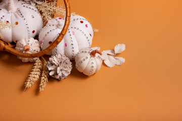 White decorative hand made pumpkins with shiny stones and pine cones in basket on colored background. Autumn harvest