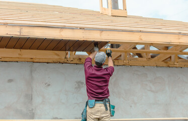 Workers install metal roofing on the wooden roof of a house.