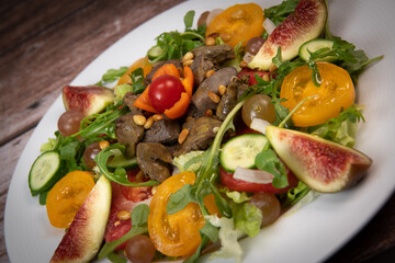 Recipe for fried chicken liver and gizzards with salad and tomatoes, cucumber, figs, grapes on a white plate, High quality photo
