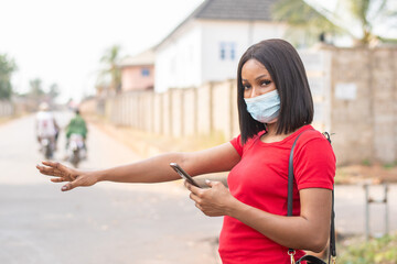 black woman wearing a face mask stopping a taxi