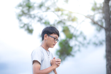Naklejka na ściany i meble Handsome boy christian in glasses. young man praying to God near a tree. concept religion. focus on face. Copy space for your individual text.