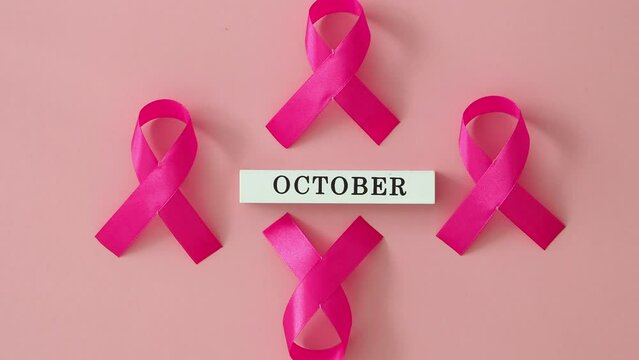 Pink ribbon symbol of breast cancer on a pink background. female hand puts the name of the month - october. Concept for International Women's Day and World Cancer Day
