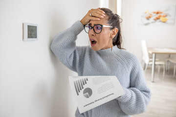 Woman cannot believe her own eyes the sum on her energy bill looking shocked at the thermostat on...