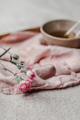 A wooden tray with a linen napkin, brewed herbal tea, pink carnations and rose quartz beads on a woolen blanket.