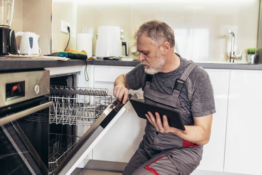Portrait Of Male Technician Repairing Dishwasher In Kitchen using digital tablet. - Powered by Adobe