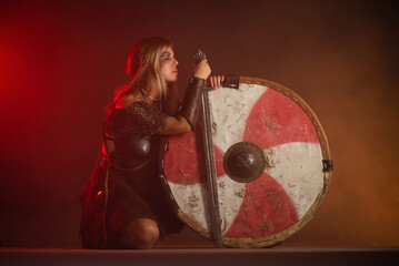 Woman warrior in the armor and with the sword and shield in hands stands on her knees. Lose the...