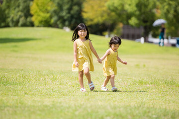 Fototapeta premium 夏の芝生の公園を手を繋いであるく小さな女の子