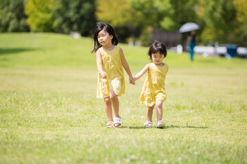 夏の芝生の公園を手を繋いであるく小さな女の子