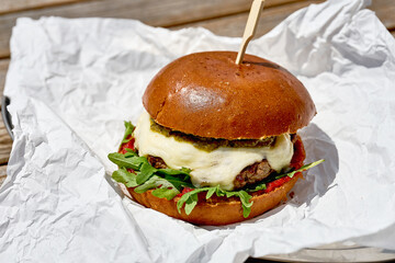 A burger with mozzarella, pesto and arugula on white parchment. Close-up, selective focus