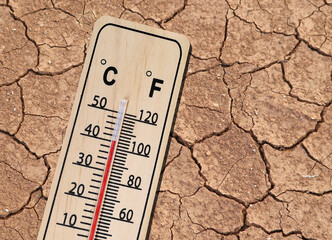 wooden thermometer shows hot temperature on dried cracked brown earth texture, concept of the...