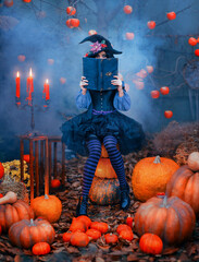 Fantasy woman halloween witch holds magic book in hands hides face sits on orange pumpkin. Festive autumn nature blue smoke red apples tree. Sexy girl. Black pointed hat purple dress striped stockings