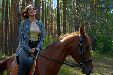 Obraz premium Woman in casual clothes rides a horse in hot summer day
