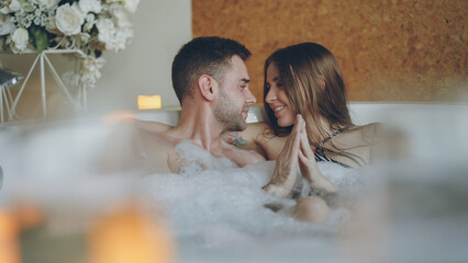 Newly married attractive couple is relaxing in jacuzzi kissing, touching hands, talking and laughing. Romantic relationship, passionate honeymoon and wellness concept. - obrazy, fototapety, plakaty
