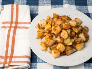 Rustic diced potato hash on white plate with colorful orange plaid napkin and blue plaid tablecloth