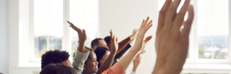 Fototapeta Active multiracial audience raising hands. Happy mixed race multiethnic people sitting in row with hands up to ask coach questions after interesting talk, session, or master class. Header background obraz