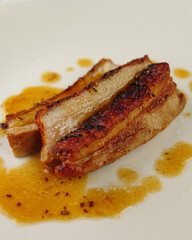 Crispy Pork Belly on a White Plate With Juices