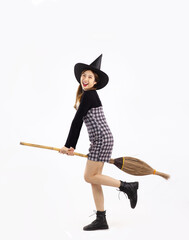 Young asian witch girl in black halloween costume wearing witch hat and holding broom smiling and...