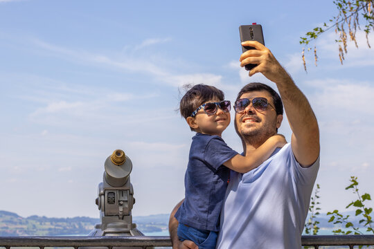 happy kid and father taking selfie on beautiful view mountains landscape summer vacation time.travel adventure family together.smiling dad and son selfie with phone camera.daddy hold in arms boy