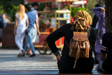 Turkish girl sits with her back with a backpack on a bench on the street in the evening. travel