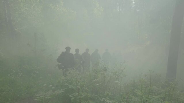 Army recruits doing basic training for a platoon attacking a battlefield with a smoke bomb in the background.