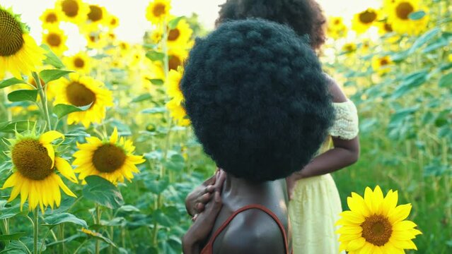 Cinematic video of an african girl with afro haircut and her daughter in a sunflowers field	